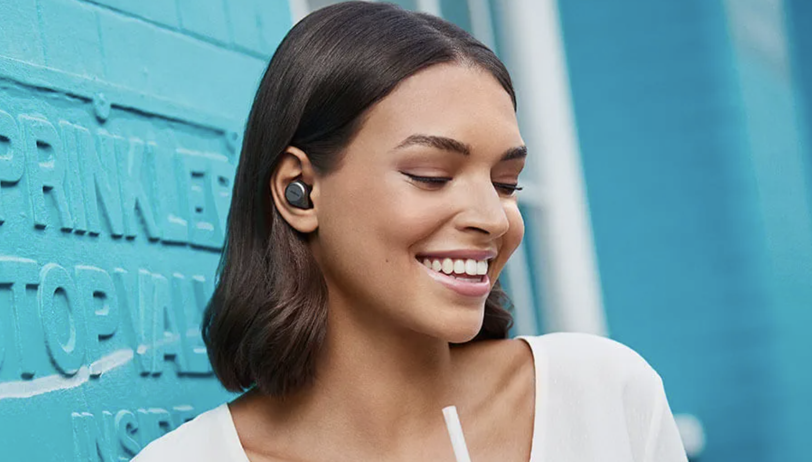 Улыбающаяся женщина носит настоящие беспроводные наушники Jabra Elite 85t.