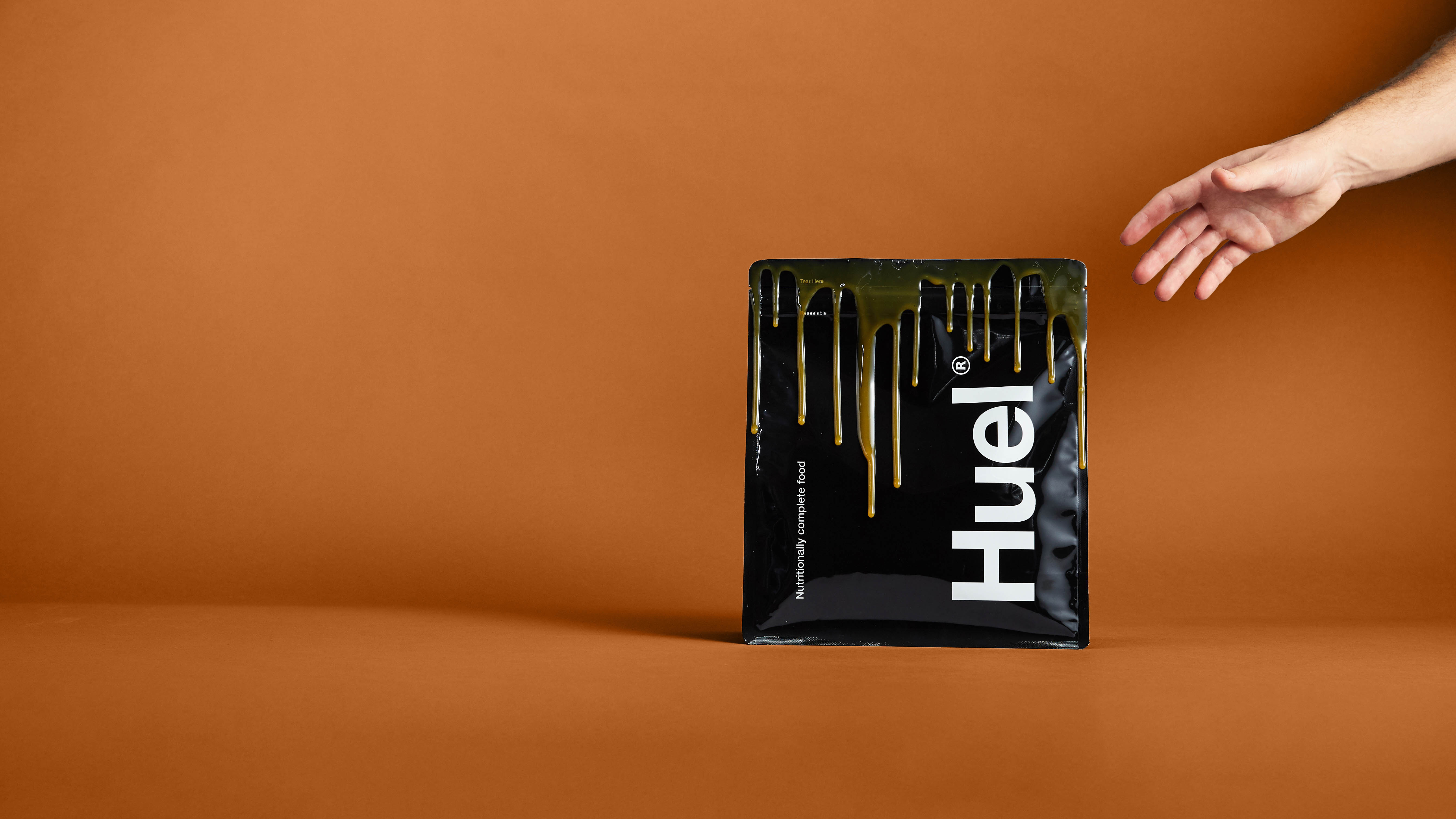 Huel Black Edition против Bulk 1 Complete Food Shake: человек тянется к пакету Huel Black Edition с карамельным соусом, капающим на боковой стороне пакета