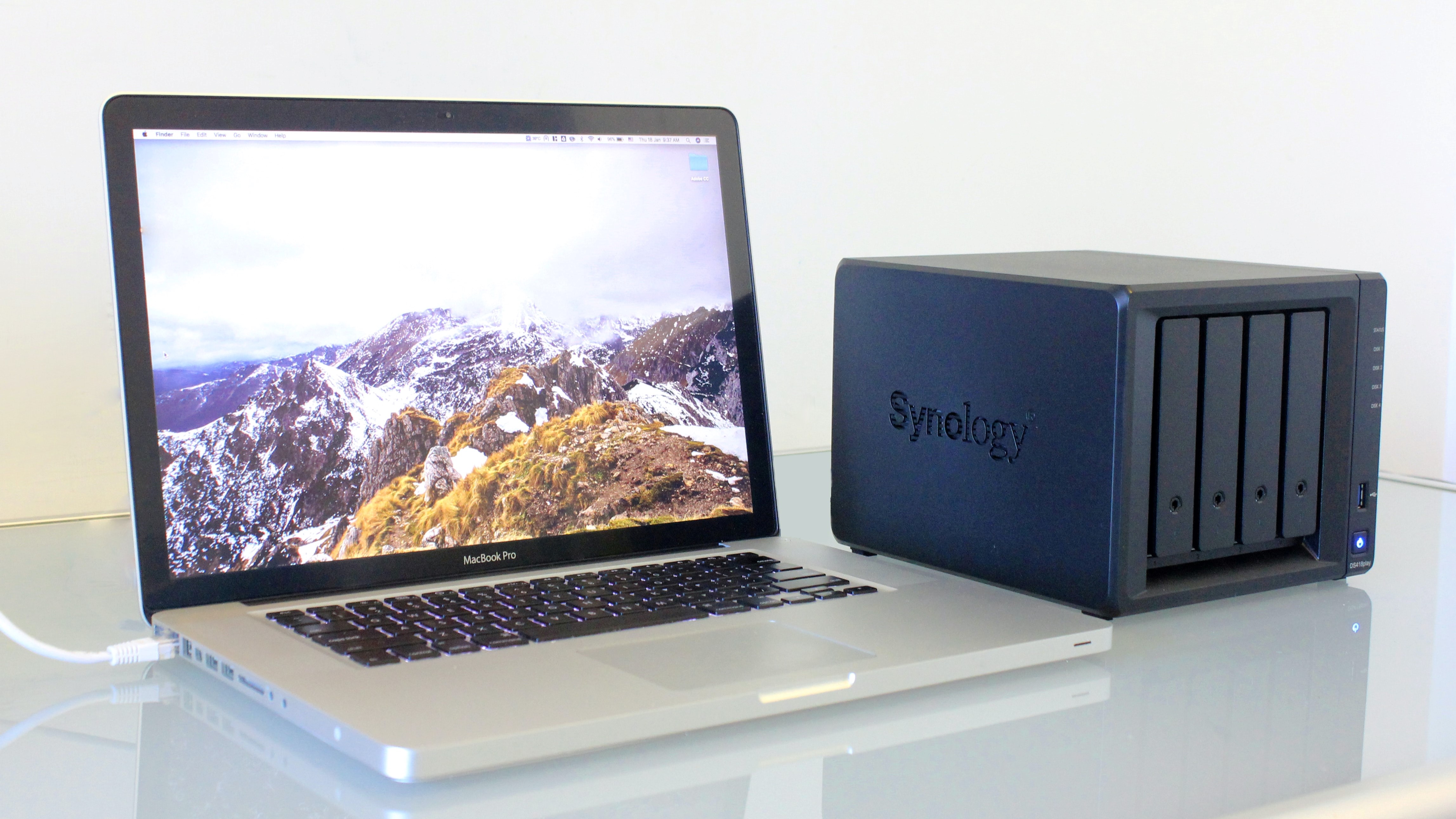 Лучшие диски NAS.  Ноутбук Apple MacBook на столе с накопителем Synology NAS