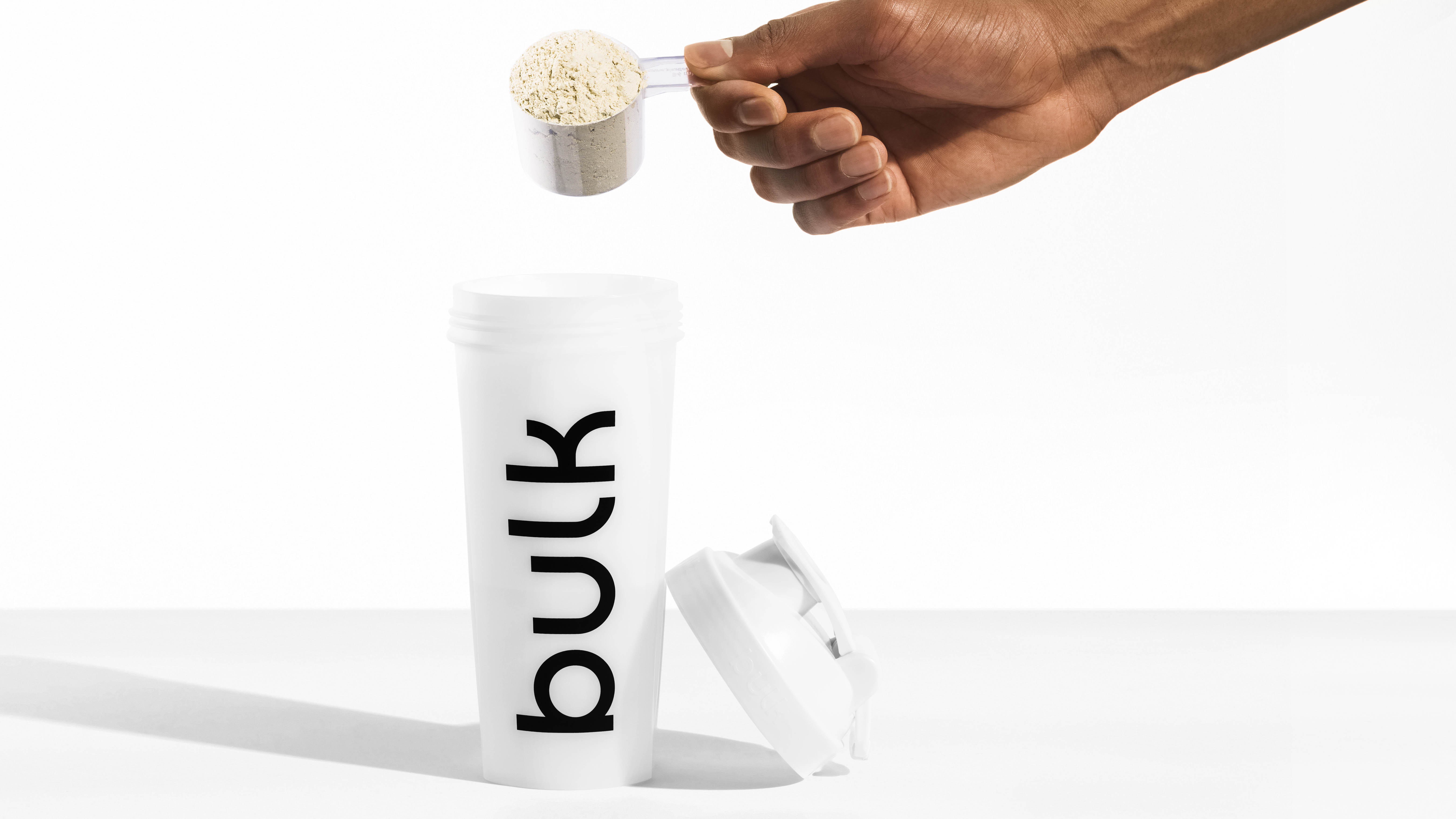 Huel Black Edition против Bulk 1 Complete Food Shake: человек опускает мерную ложку Bulk 1 в шейкер, стоящий на столе