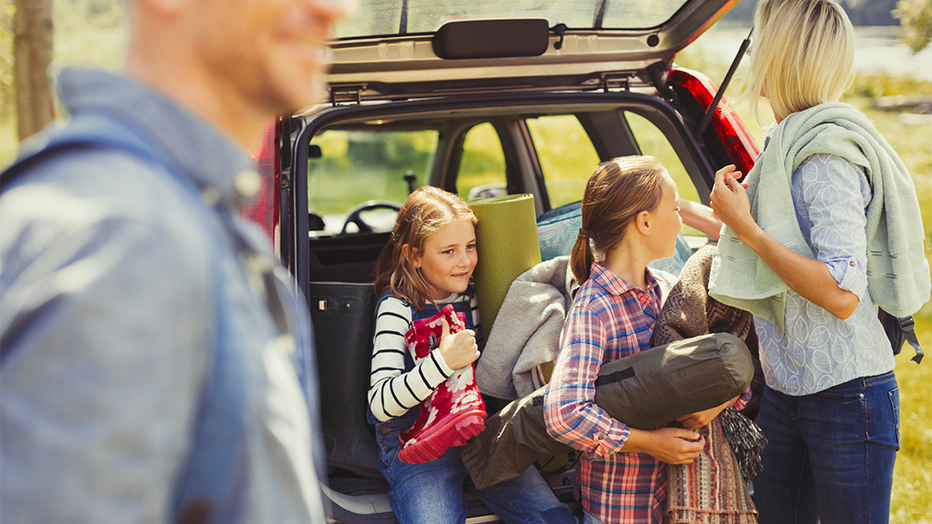 Кемпинг с детьми: семья выгружает походное снаряжение из багажника машины