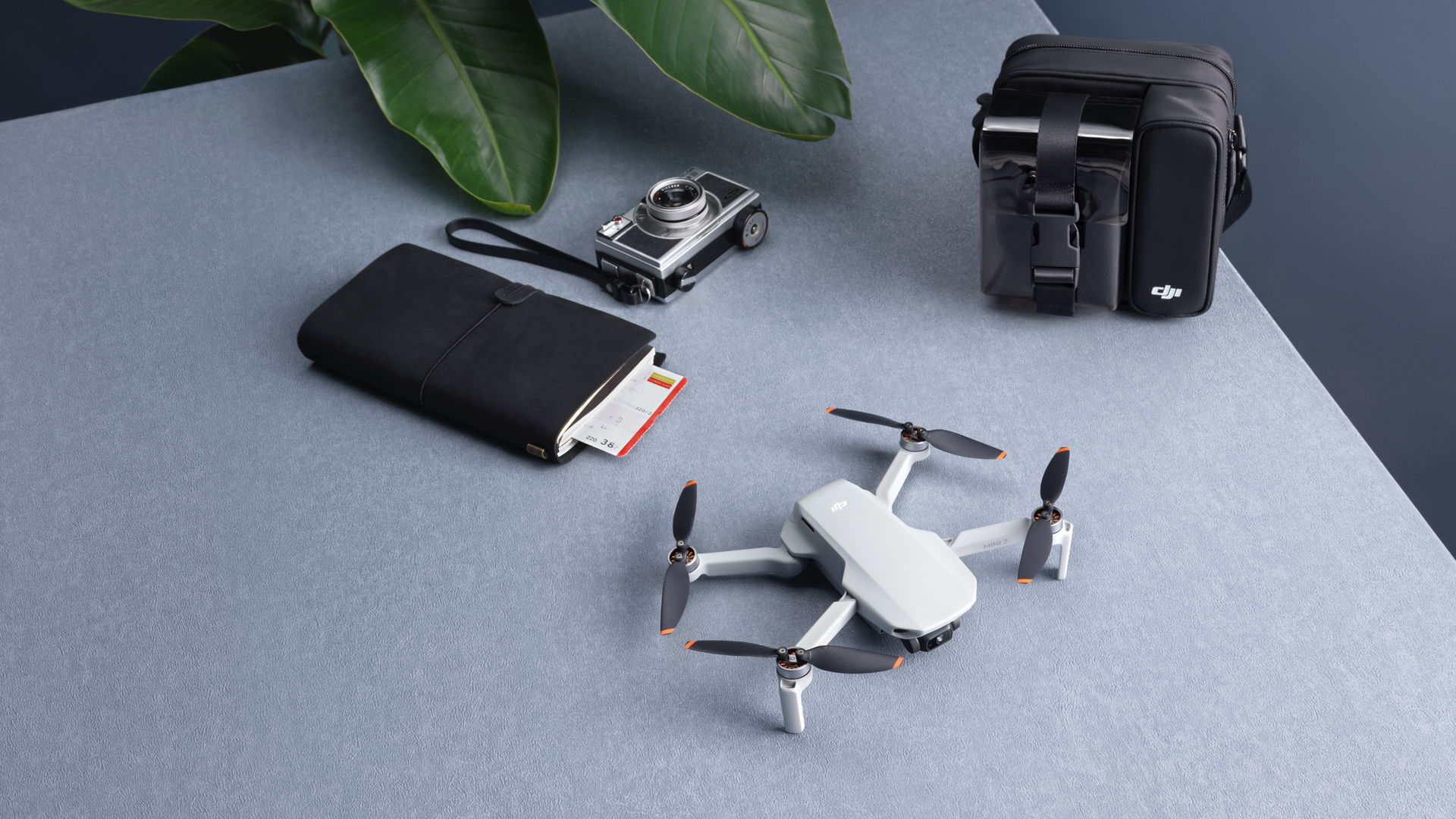 Дрон DJI Mini 2 на столе рядом с дневником, камерой и сумкой