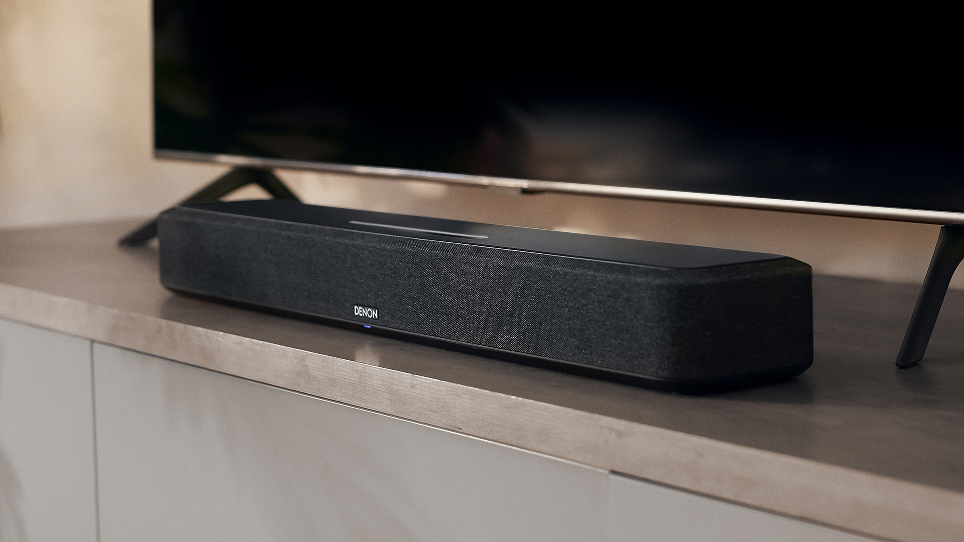 Denon Home Sound Bar 550 перед телевизором на деревянной поверхности