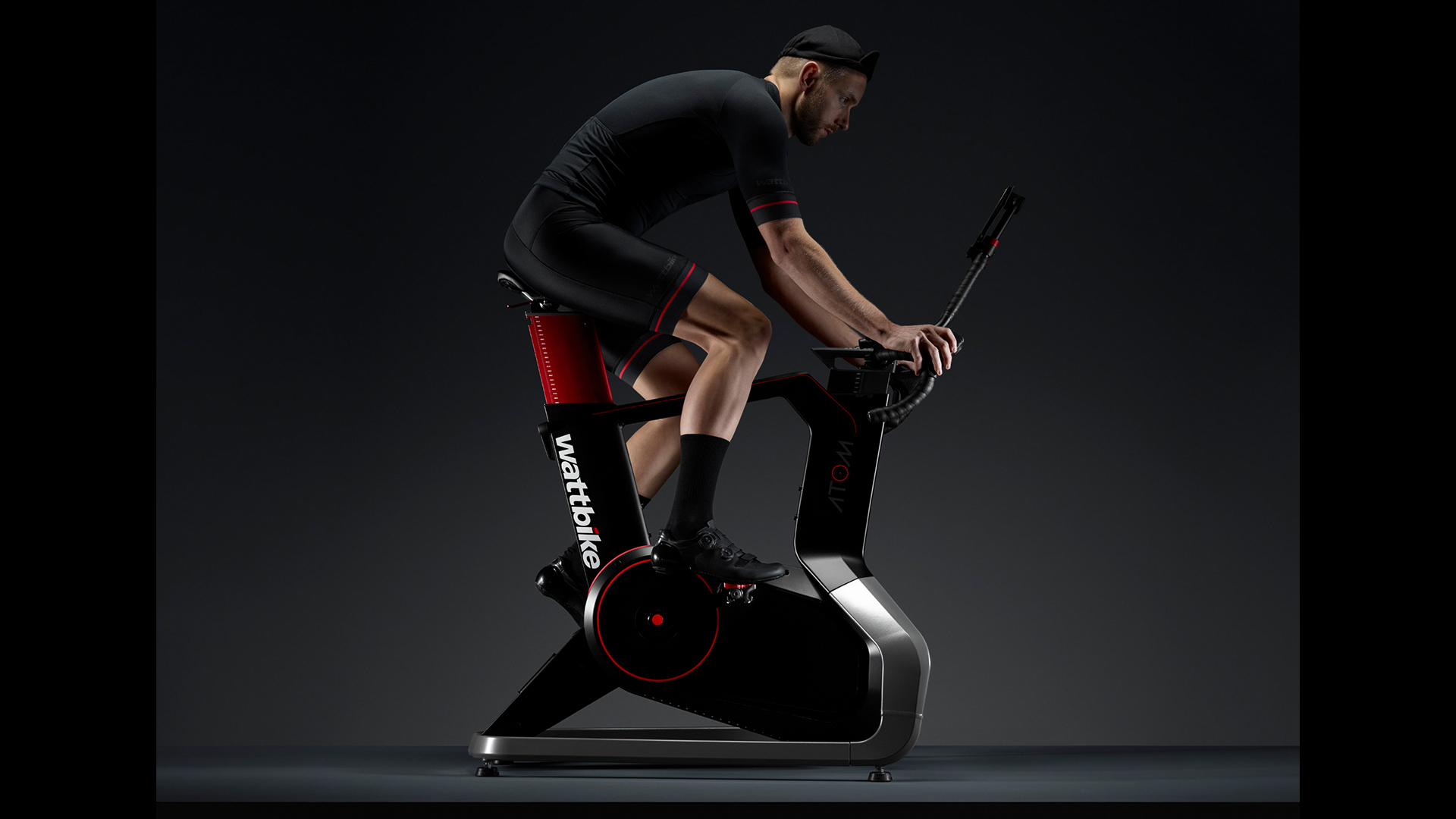 Обзор Wattbike Atom: на фото молодой человек катается на велотренажере в темной фотостудии.