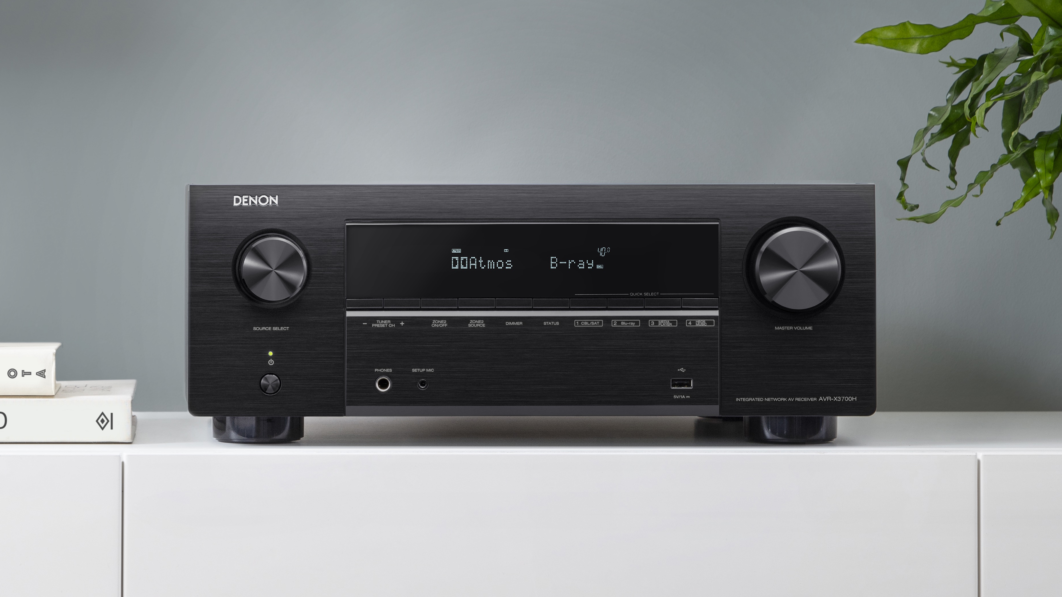 Обзор Denon AVC-X3700H, показывающий продукт, стоящий на белой полке в гостиной.