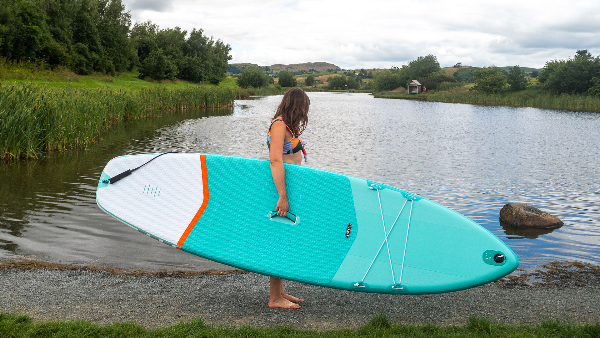 Женщина держит Decathlon X100 SUP на доске для гребли рядом с озером