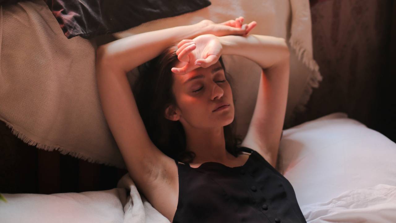 Женщина спит в постели с руками над головой, советы по сну и хорошему самочувствию