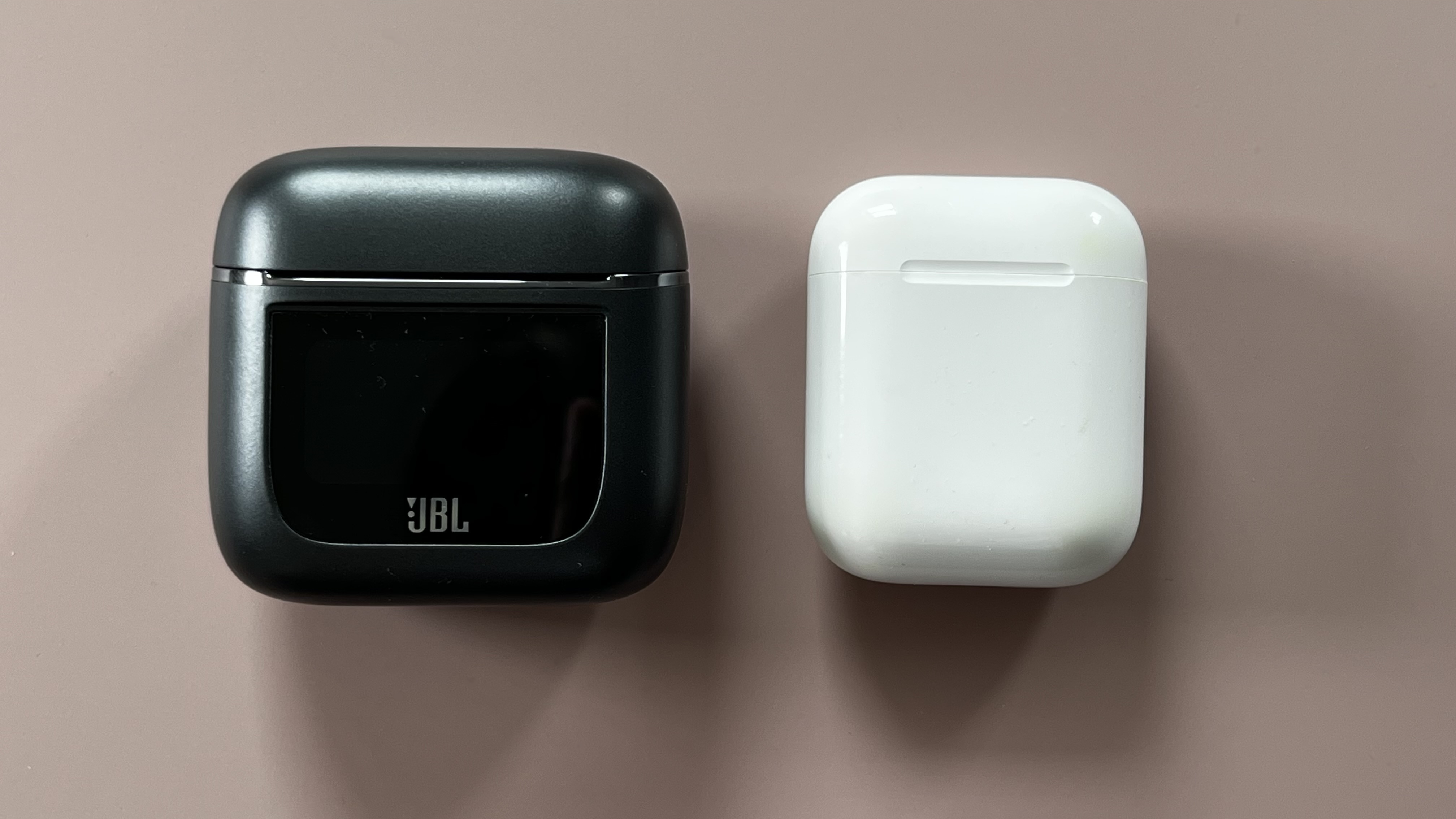 Наушники JBL Tour Pro 2 на розовом фоне рядом с Apple Airpods для сравнения